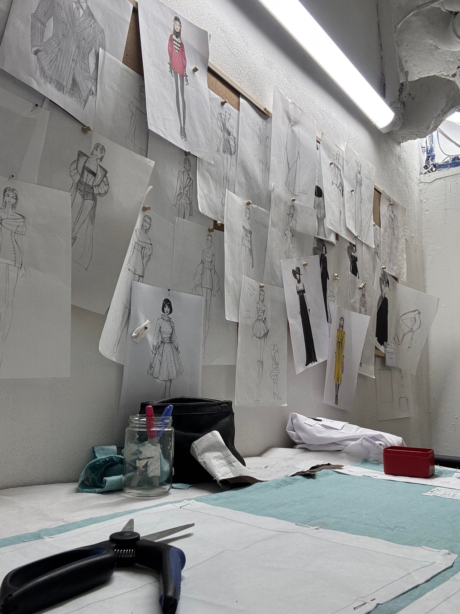 Bozzetti di abiti disegnati a mano, appesi alla parete del laboratorio